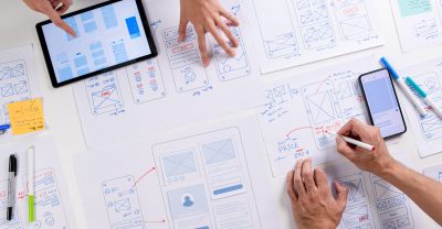 UX/UI designers discussing and brainstorming on wireframes for a website and mobile app prototype, surrounded by sketches of user flow and design tools, in the concept of website and mobile application design concept.